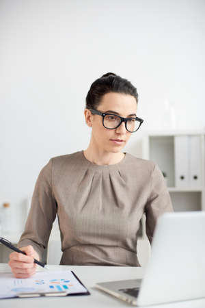 Mid age businesswoman working with documents on a laptop in the officeの写真素材