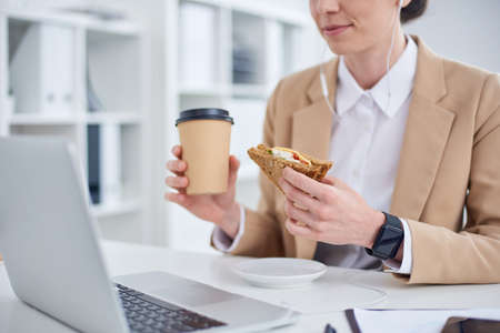 Mid age businesswoman having lunch at laptop in the officeの写真素材