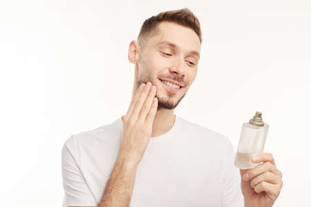 Smiling man wearing perfume on white background