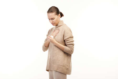 Ill woman in beige sweater has thore troat and holds a napkin.