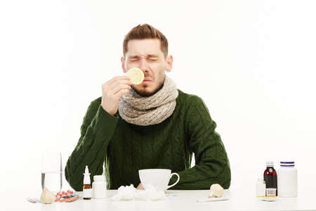 Ill man in green sweater sniffs a lemon from a tea cup.