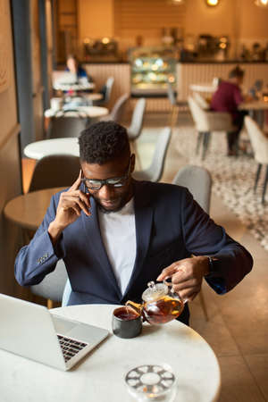 Afro-american working at the laptop and pouring himself tea.の写真素材