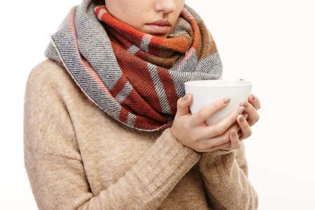 Close-up of an ill woman drinking hot tea in a white mug.