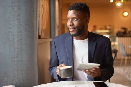 Man in a dark suit drinks tea from a big cup.
