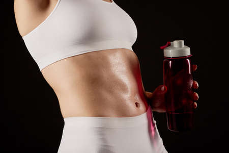 Close up of a woman in sportswear showing her six-pack at the camera and holding a water bottle.