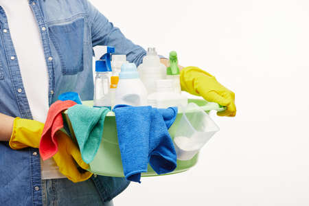 Close up of a woman in work-wear holding a big green bucket full of cleaning supplies and rags.
