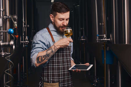 Tattooed man tastes beer from the glass he holds.の写真素材