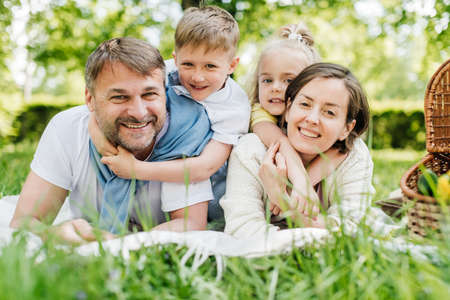 Mom and dad laying on the grass holding their children.