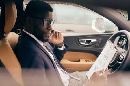 Businessman in a suit sits in a car and talks on the phone.
