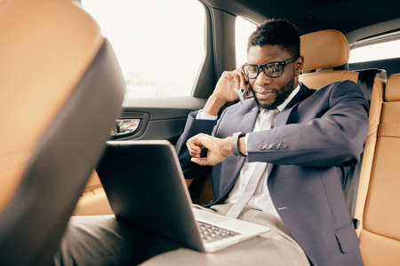 Man talking on the phone during car ride with a laptop nearby.の写真素材
