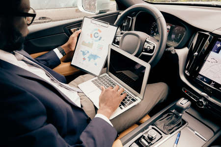 Businessman working on the laptop and looking at the notepad he holds as part of his work related...