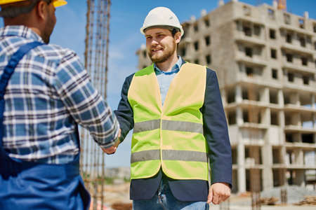 Two male engineers shake each others hands friendly.