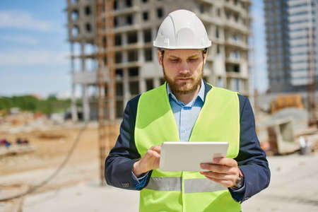 An engineer works on his tablet at the construction spot.