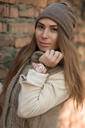 Beautiful woman in a knitted garment and cap at brick wallの写真素材