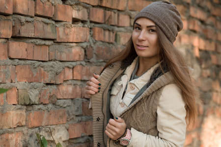 Beautiful woman in a knitted garment and cap at brick wallの写真素材
