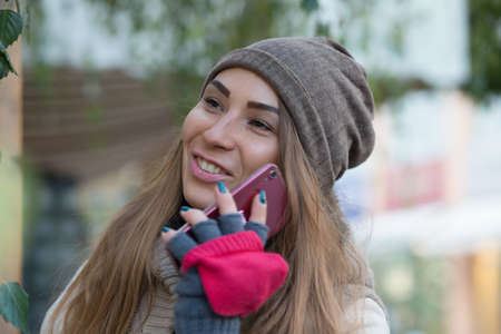 Woman in knitted garment, cap and gloves speak by phone in city.の写真素材