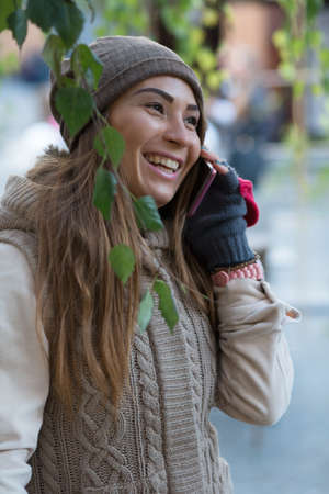 Woman in knitted garment, cap and gloves speak by phone in city.の写真素材