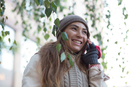 Woman in knitted garment, cap and gloves speak by phone in city.の写真素材