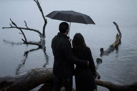 Couple stand back under an umbrella near the riverの写真素材