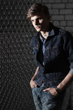 Stylish man in denim jacket standing near steel gridの写真素材