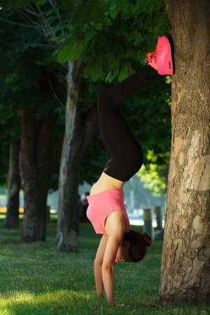 Pretty sportswoman doing exercises in outdoor park setting, green trees backgroundの写真素材