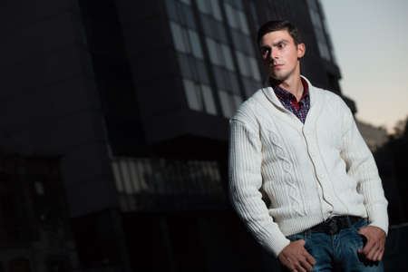 Fashion photo of stylish man in white pullover. Building background.の写真素材