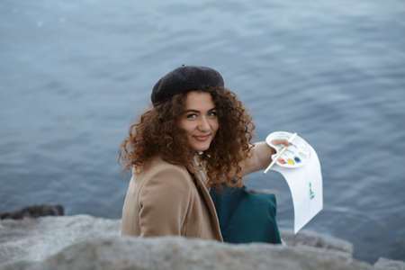 Woman drawing picture near river and smile