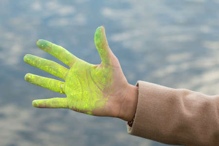 Woman's hand colored by bright yellow paint. River background.の写真素材