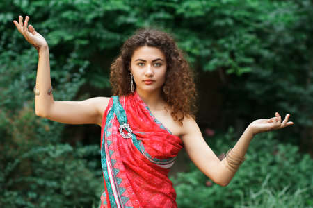 Portrait of Indian girl in sari with pattern of henna on hands. Green trees background.の写真素材