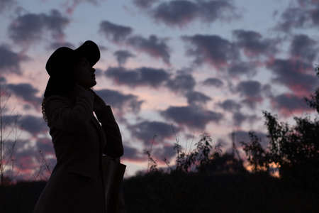 Silhouette of woman in hat in evening twilightの写真素材