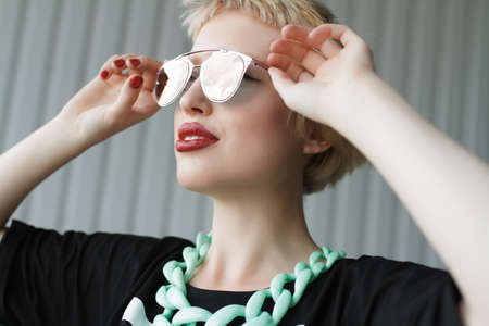 Closeup girl portrait. Woman holding sunglasses. Profiled sheeting wall background. The strange urban fashion photographyの写真素材