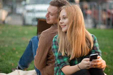 The couple sit back together on the grass in parkの写真素材