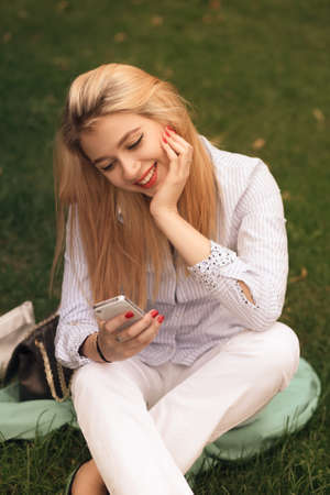 Girl sitting on the grass with phone and smiling
