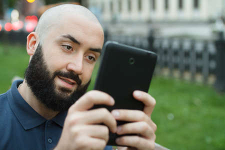 Bearded bald man sitting on a bench and game on tablet at the alleyの写真素材