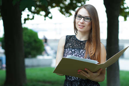 Business woman in the glasses with folder and paper notebook standing in the park on conferenceの写真素材