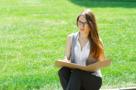 Business woman with folder and paper notebook sitting in the park on conference and read articleの写真素材
