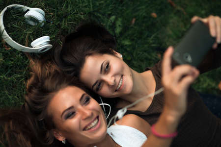 Girlfriends taking picture with smartphone lying on the grassの写真素材