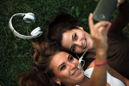 Girlfriends taking picture with smartphone lying on the grassの写真素材