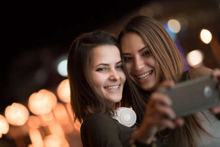Girlfriends taking self picture with smartphoneat night city