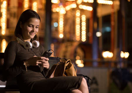 Woman sitting on a bench in town with the phoneの写真素材