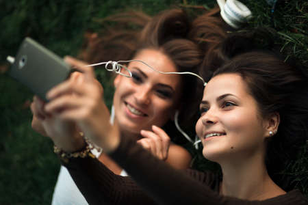 Girlfriends taking picture with smartphone lying on the grassの写真素材
