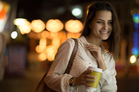 Pretty girl in the night city drinking coffee. City lights.の写真素材
