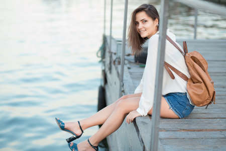 Beautiful girl sitting on the berth near riverの写真素材