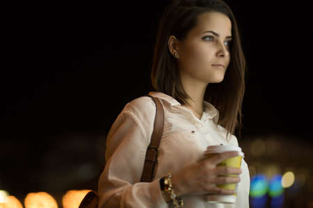 Pretty girl in the night city drinking coffee. City lights.の写真素材