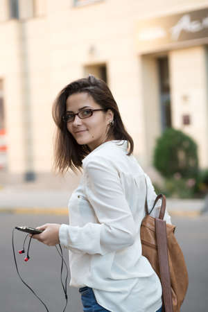 Pretty girl with backpack and phone walking in city street.の写真素材