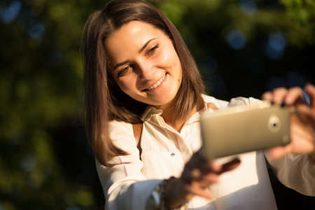 Pretty girl take photo on her smartphone in park.の写真素材