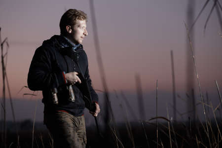Huntsman with rifle standing on guard in field in twilight