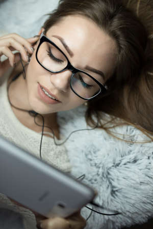 Cute woman lies on bed with tablet and listen music