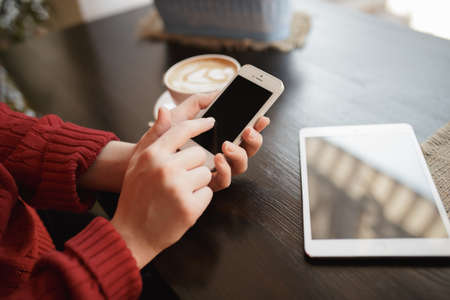 Woman's hand using a while cellphone sitting in coffee shopの写真素材