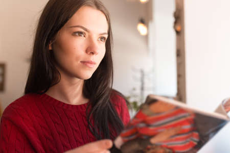 Woman in red pullover reading journalの写真素材